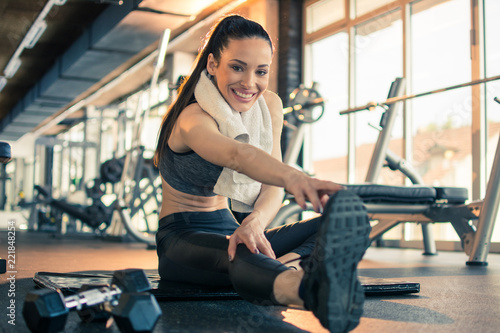 Smiling fitness girl touching toes and stretching her hands and legs at gym