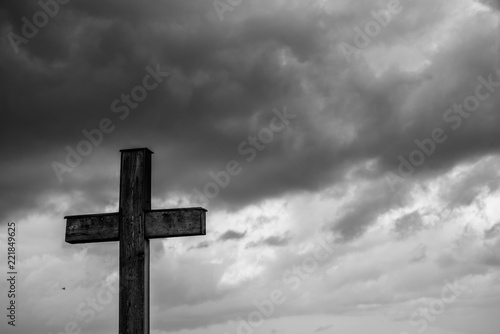 Simple oak catholic cross, storm clouds in the background, space for text in black and white.