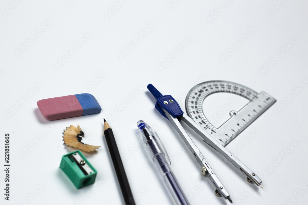 A close-up photo of stationary set: pen, pencil, compass, rubber, protractor and etc. on the white background on the table in office, school or university. A workspace of student or an office worker.
