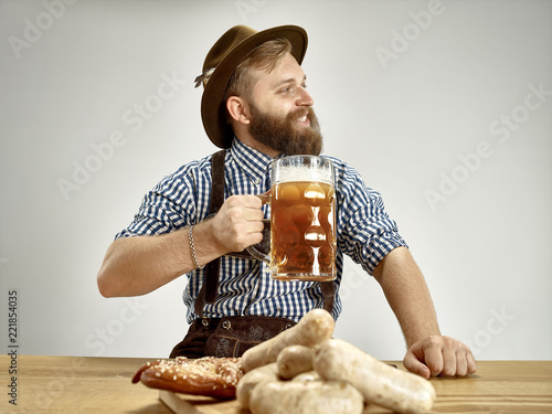 Germany, Bavaria, Upper Bavaria. The young smiling man with beer dressed in traditional Austrian or Bavarian costume in hat holding mug of beer at studio