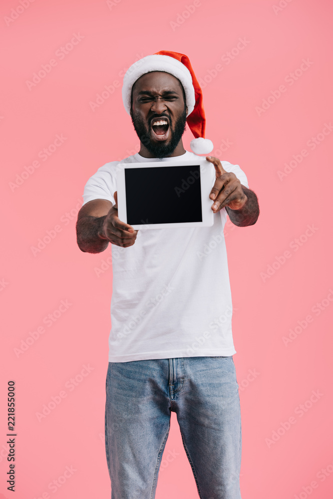 portrait of emotional african american man in santa claus hat with tablet with blank screen isolated on pink portrait of emotional african american man in santa claus hat with tablet with blank screen isolated on pink