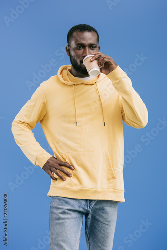 confident young african american man drinking coffee from paper cup isolated on blue background