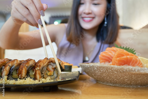 Woman holding a sushi with chopsticks to eat.