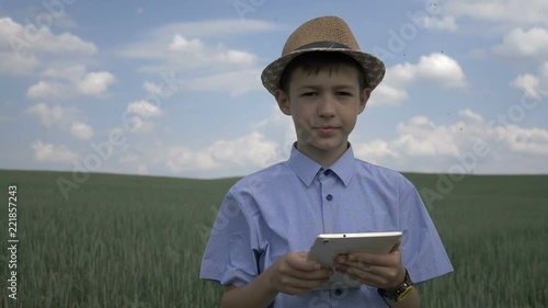 farmer boy in a hat uses a tablet in the field, checks the crop photo