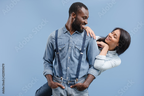 smiling african american couple hugging and looking at each other isolated on blue