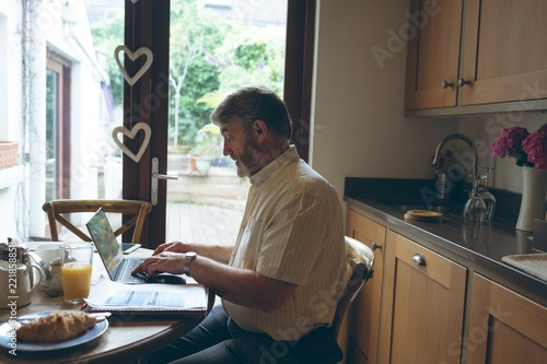 Senior man using digital tablet on dining tablet at home photo