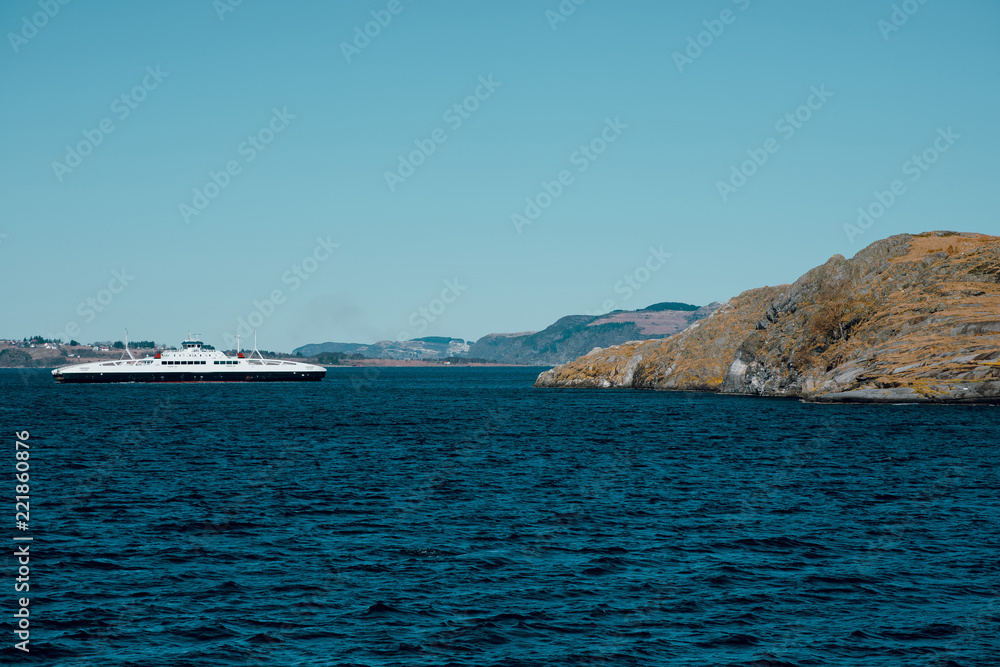 Beautiful landscape of cold fjord and island with small houses. Ferry boat in the sea. Sunny winter day in Norway.
