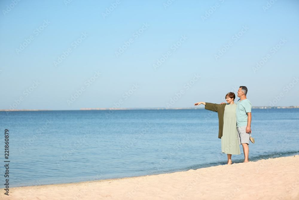 Happy mature couple walking at beach on sunny day