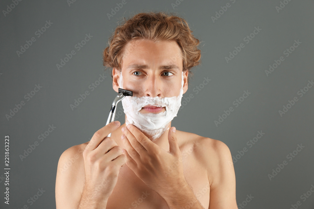 Handsome young man shaving on gray background Handsome young man shaving on gray background