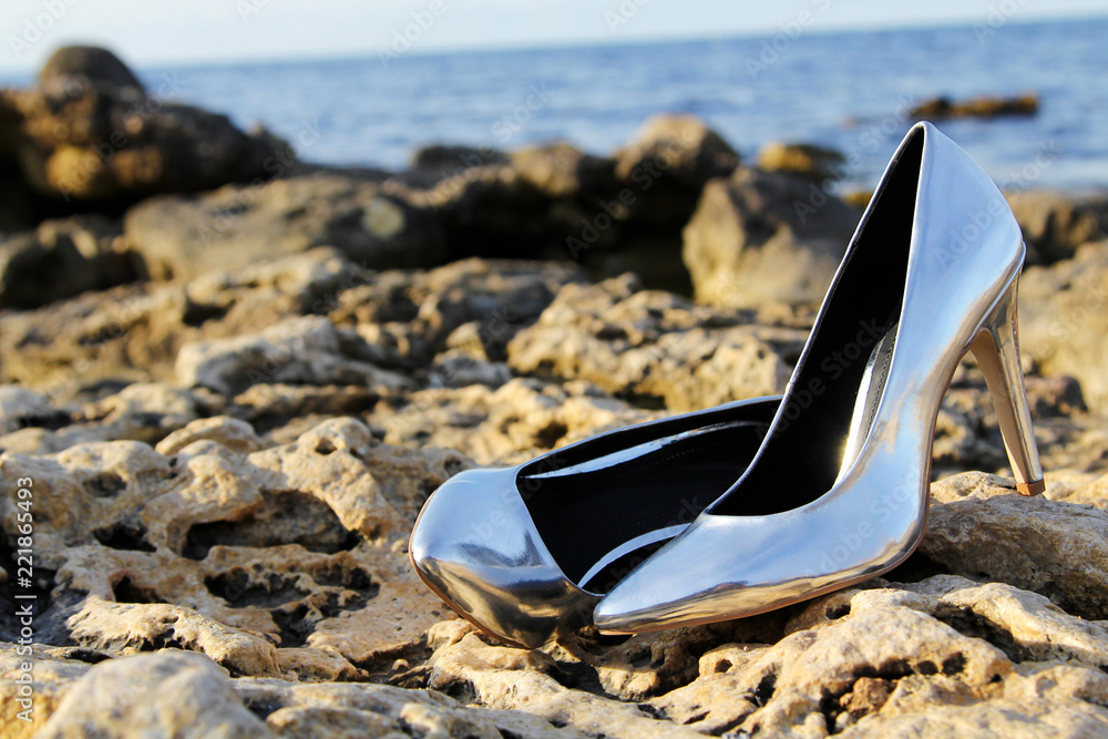 Close-up shot of Pair of Silver High Heel Shoes on yellow stones near sea Close-up shot of Pair of Silver High Heel Shoes on yellow stones near sea