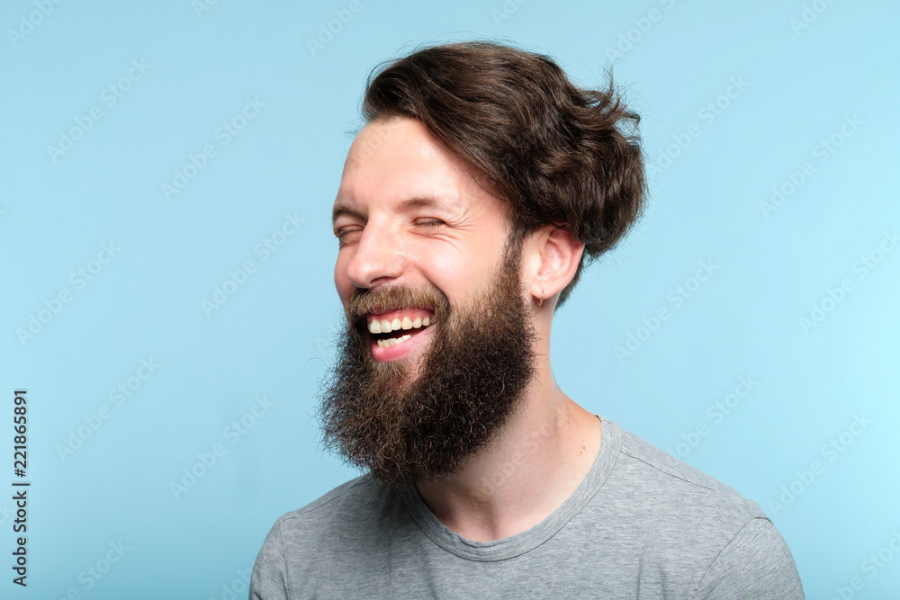 Fototapeta premium emotional facial expression. happy joyful smiling man. young handsome bearded hipster guy portrait on blue background.