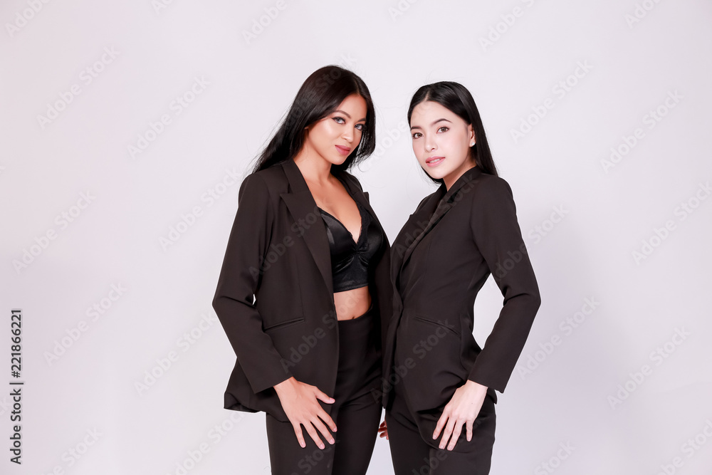 Two Asian fashionable charming female models in black suit and pants standing and posing together isolated over white background. Two Asian fashionable charming female models in black suit and pants standing and posing together isolated over white background.