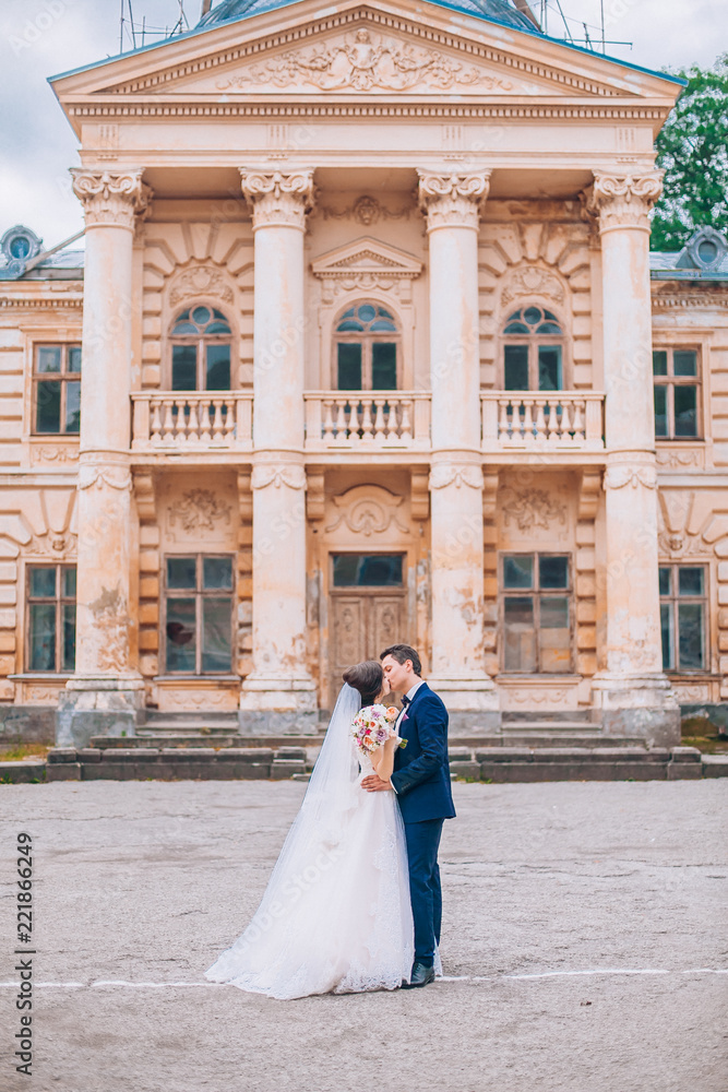 Obraz premium Wedding in the castle. Stylish and beautiful. Princess's dress. Lush white dress and veil. Bride is a brunette. The groom in a black suit. A couple is walking near the castle grounds.