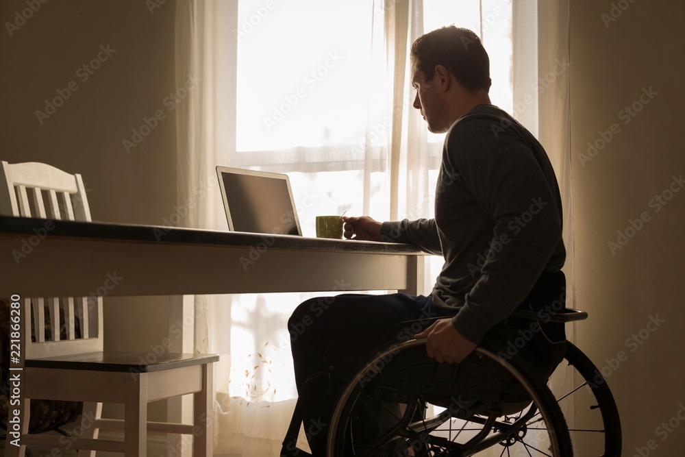 Disabled man having coffee while using laptop on dinning table Disabled man having coffee while using laptop on dinning table