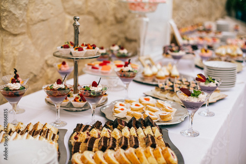 Candy bar. White wedding cake decorated by flowers standing of festive table with deserts, strawberry tartlet and cupcakes. Wedding. Reception Tartlets © nataliakabliuk