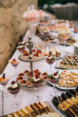 Candy bar. White wedding cake decorated by flowers standing of festive table with deserts, strawberry tartlet and cupcakes. Wedding. Reception Tartlets © nataliakabliuk