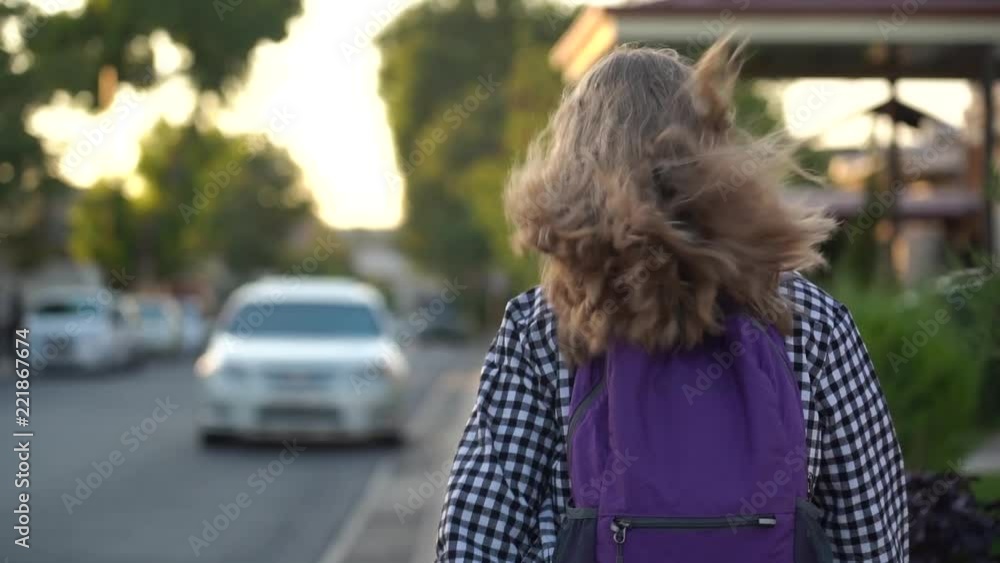 Girl is walking to school on the sidewalk in white sneakers with a purple of backpack. Slow motion video. Girl is walking to school on the sidewalk in white sneakers with a purple of backpack. Slow motion video.