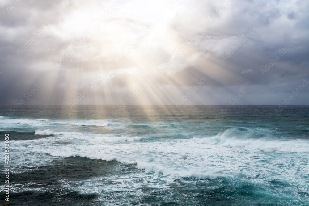 Rays of sunlight break through storm clouds above the open ocean waves in a heavenly seascape