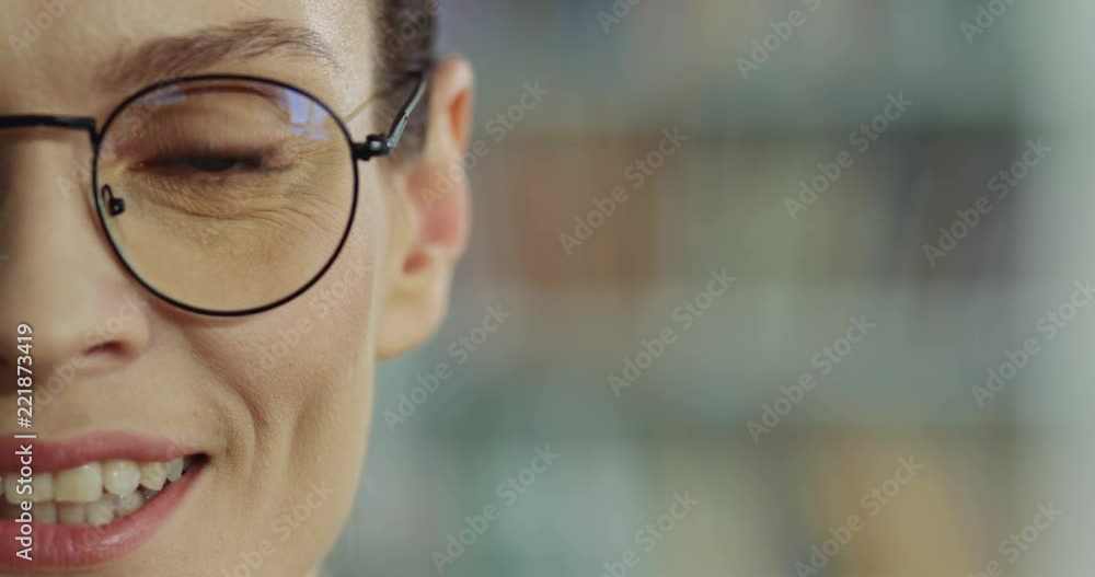 Close up of the Caucasian good looking woman's half face in the glasses smiling joyfully on the blurred background. Close up of the Caucasian good looking woman's half face in the glasses smiling joyfully on the blurred background.
