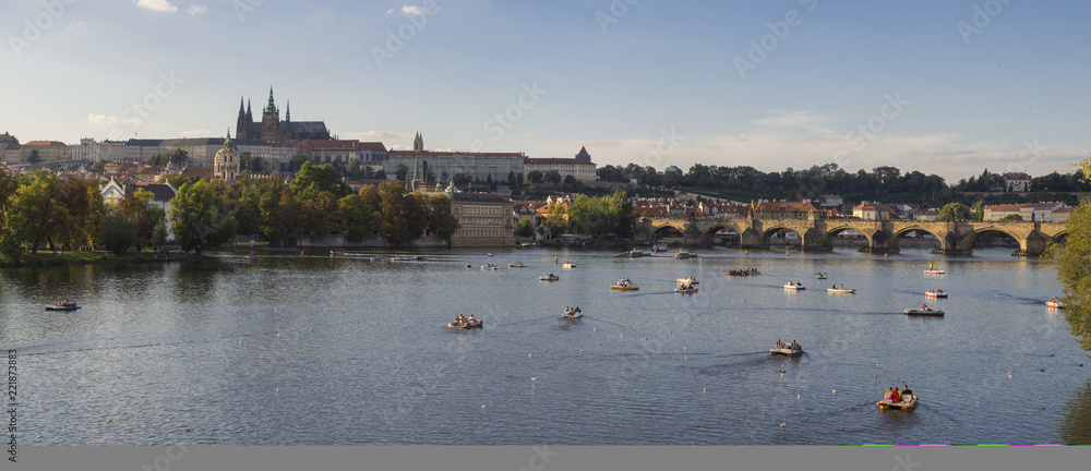 Wide panorama of Charles bridge over Vltava river and Gradchany, Prague Castle and St. Vitus Cathedral. Czech Republic, panoramic view, golden hour light, summer day, tourists on boats