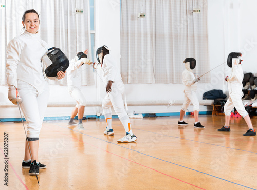 Portrait of smiling sporty young woman with foil at fencing workout