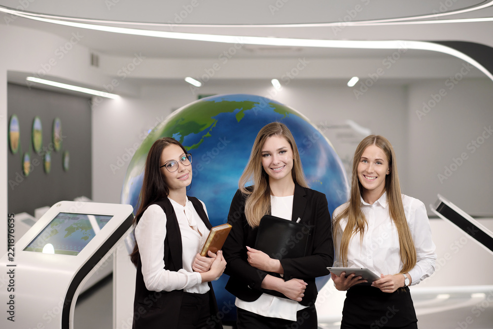 Three beautiful young girls in the office with a tablet on the background of the globe. Business and science.