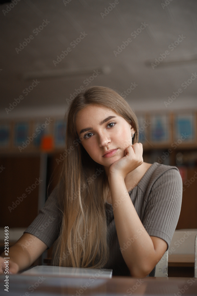 Thinking beautiful young student schoolgirl lady with long hair looking camera sitting at the table in classroom with copybook. Thinking beautiful young student schoolgirl lady with long hair looking camera sitting at the table in classroom with copybook.