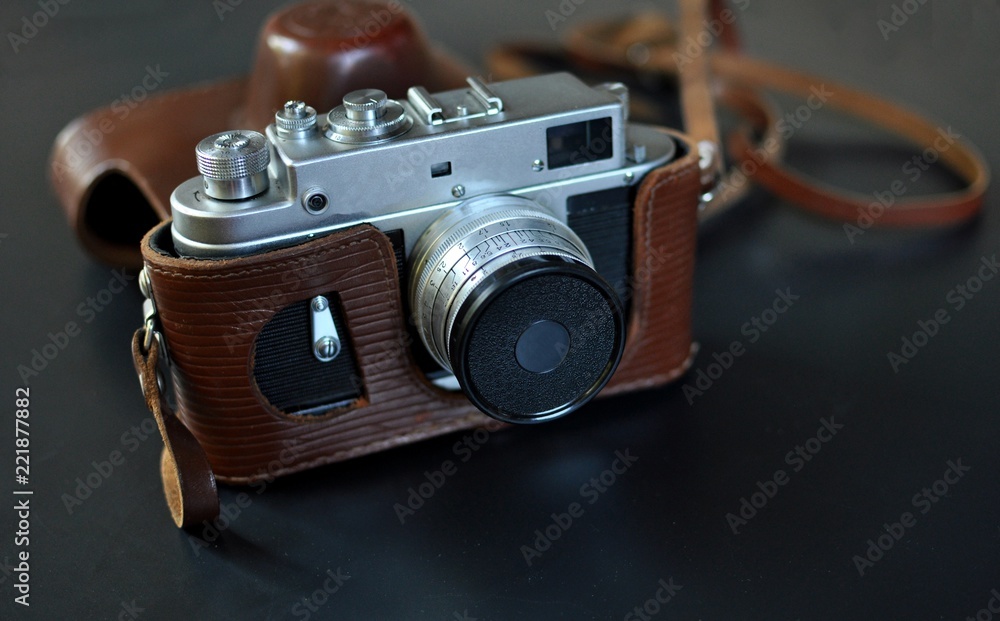 Vintage old film camera with brown leather case, on black background