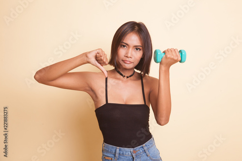 Unhappy Asian woman thumbs down with dumbbells.