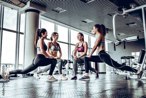 Vászonkép Four athletic woman performing low fallouts in gym with panoramic windows backgr