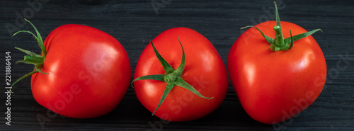 red tomatoes on a green branch on a black wooden background