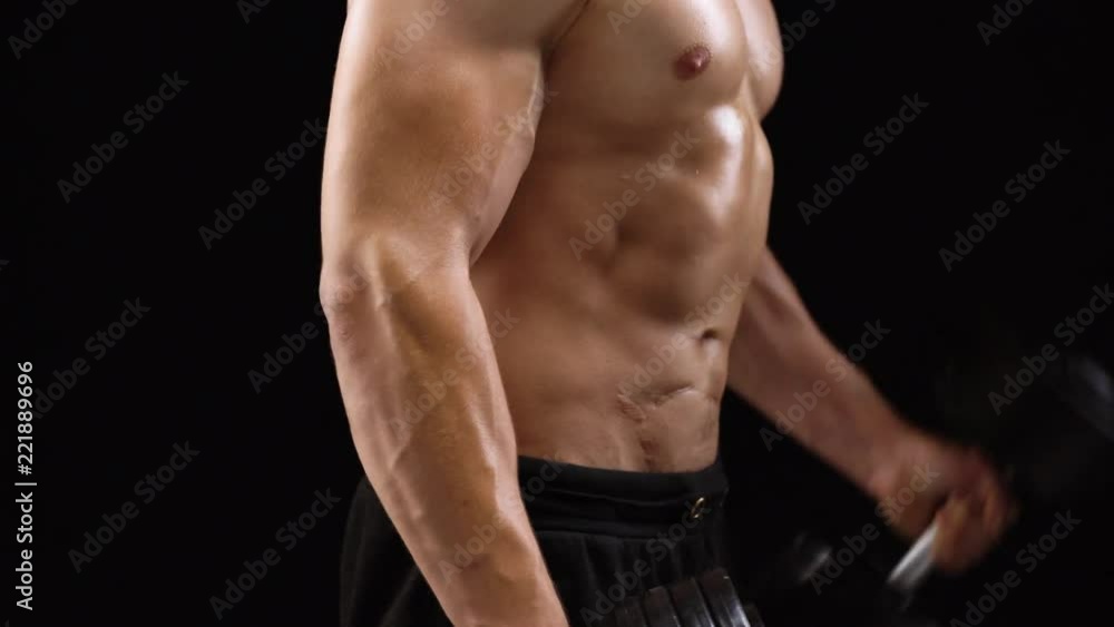 Man flexes his hands with dumbbells, training his biceps on a black background in the studio Man flexes his hands with dumbbells, training his biceps on a black background in the studio