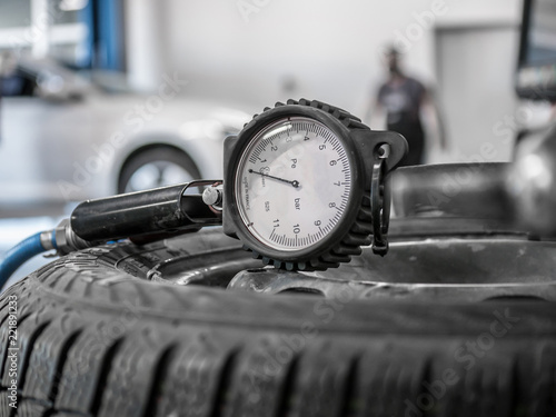 Close up tire and checking air pressure with gauge pressure in service station. Tire pressure gauge on the wheel. White car in background. Tire pressure gauge closeup.