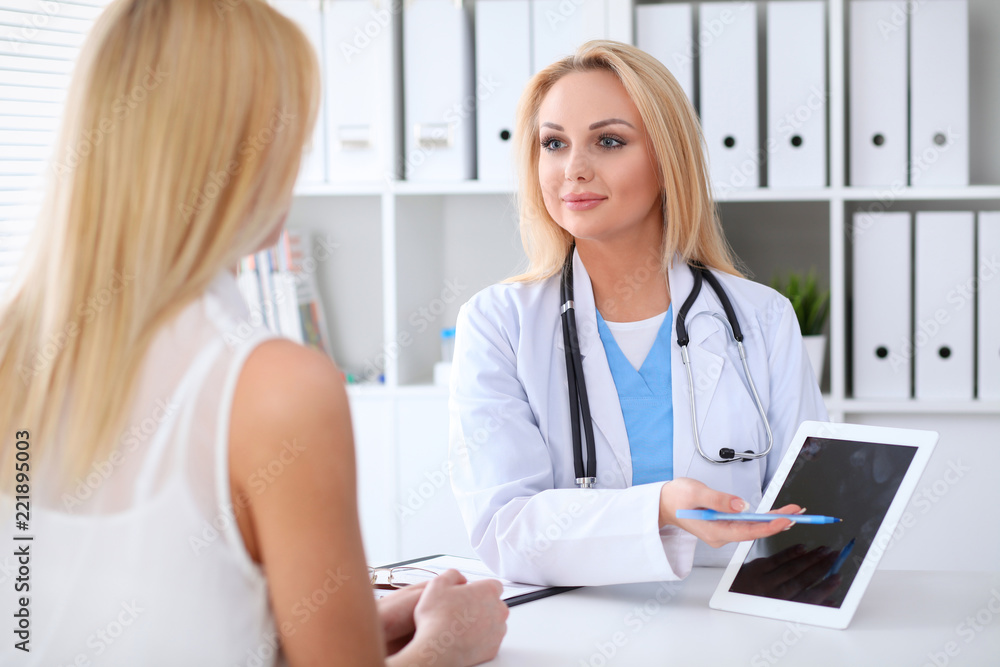 Doctor and patient discussing something while sitting at the table at hospital. Physician using tablet pc for information demonstration. Medicine and health care concept Doctor and patient discussing something while sitting at the table at hospital. Physician using tablet pc for information demonstration. Medicine and health care concept