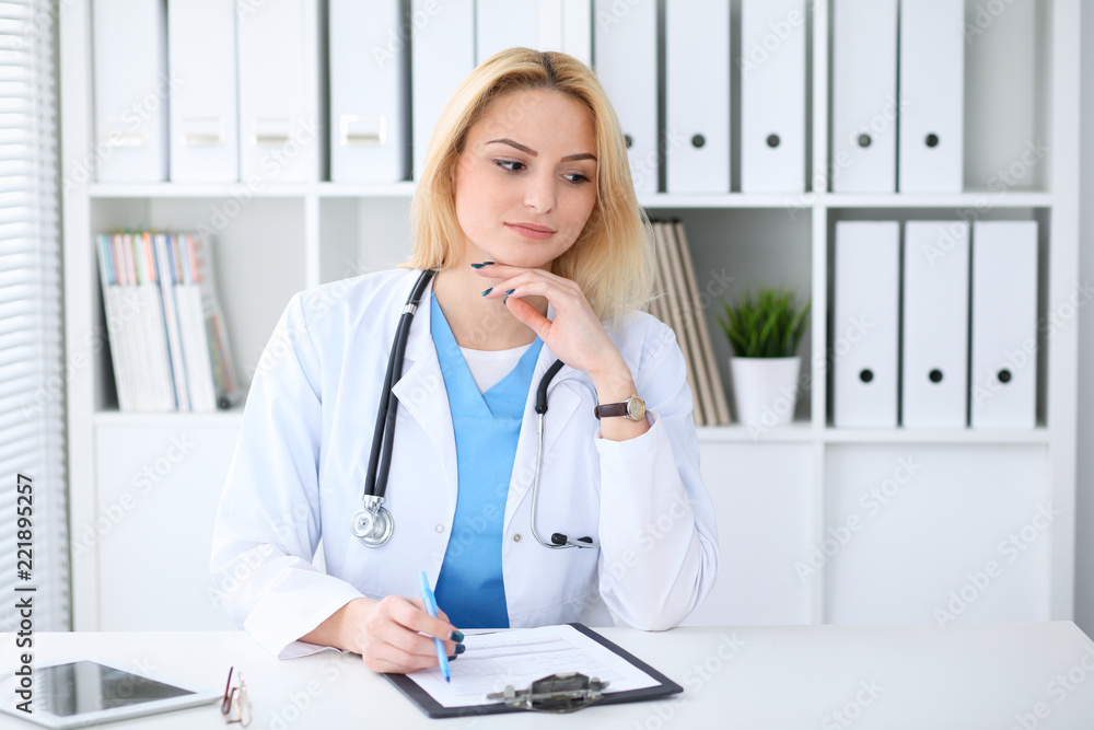 Doctor woman at work. Portrait of cheerful smiling blonde physician sitting at the desk. Medicine and healthcare concept Doctor woman at work. Portrait of cheerful smiling blonde physician sitting at the desk. Medicine and healthcare concept