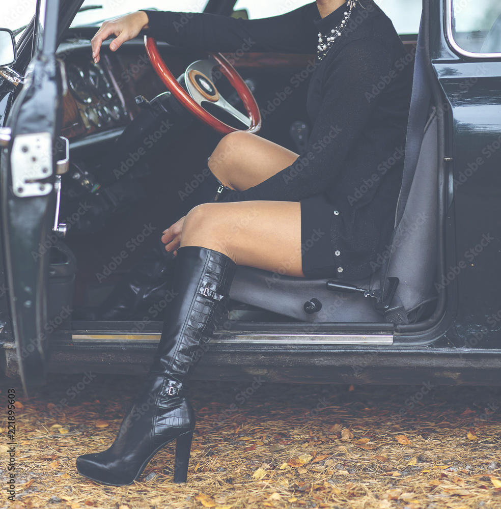 Sexy lady sitting in a classic car. Long leather boots and black