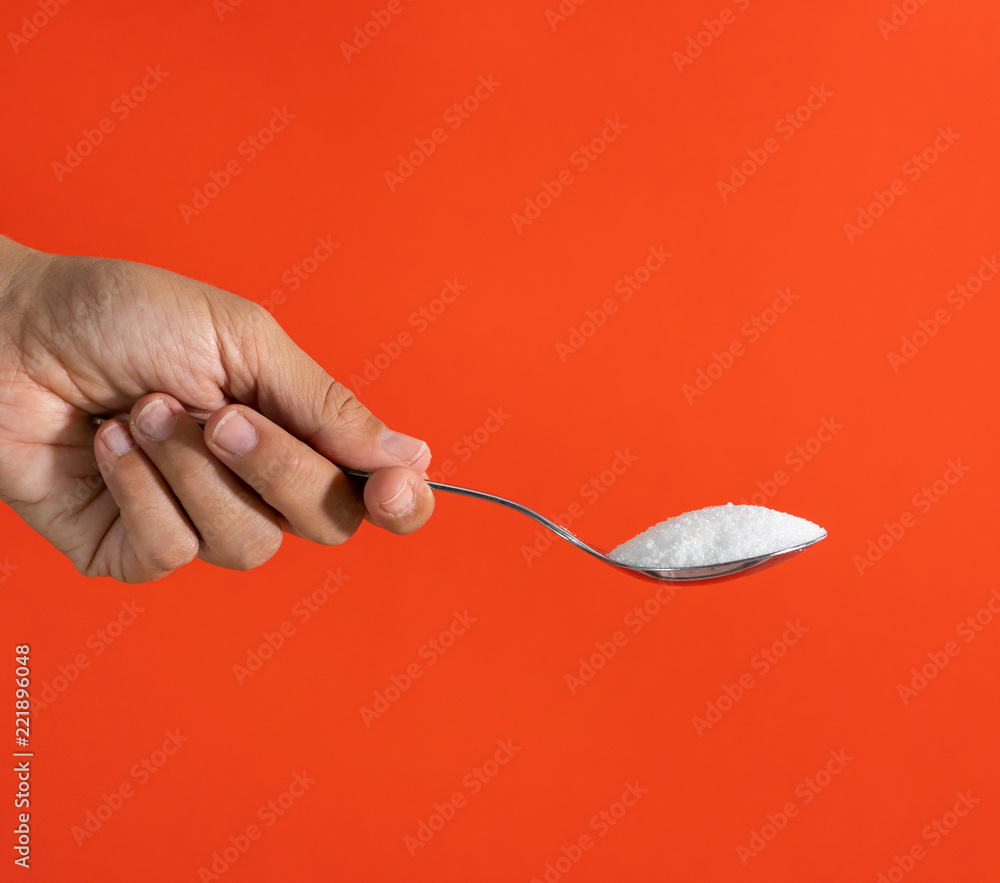 Woman hand holding and offering a spoon full of sugar isolated on a red background in sugar addiction, diet, health problems, diabetes, calories and quantity of sugar in products concept Woman hand holding and offering a spoon full of sugar isolated on a red background in sugar addiction, diet, health problems, diabetes, calories and quantity of sugar in products concept