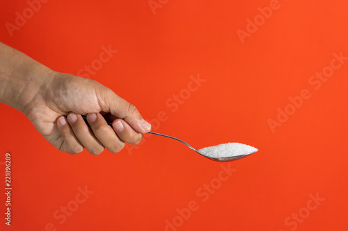 Woman hand holding and offering a spoon full of sugar isolated on a red background in sugar addiction  diet  health problems  diabetes  calories and quantity of sugar in products concept