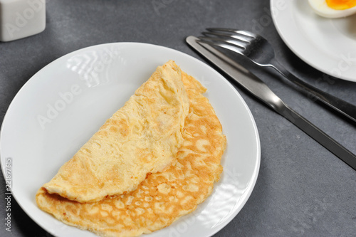 Omelette from chicken eggs on a white plate. Next to the plate are cutlery. Gray background. View from above. Close-up. Macro photography.