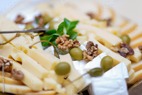 Close up photo of cheese platter with selection of various cheese served with walnuts and green olives photo