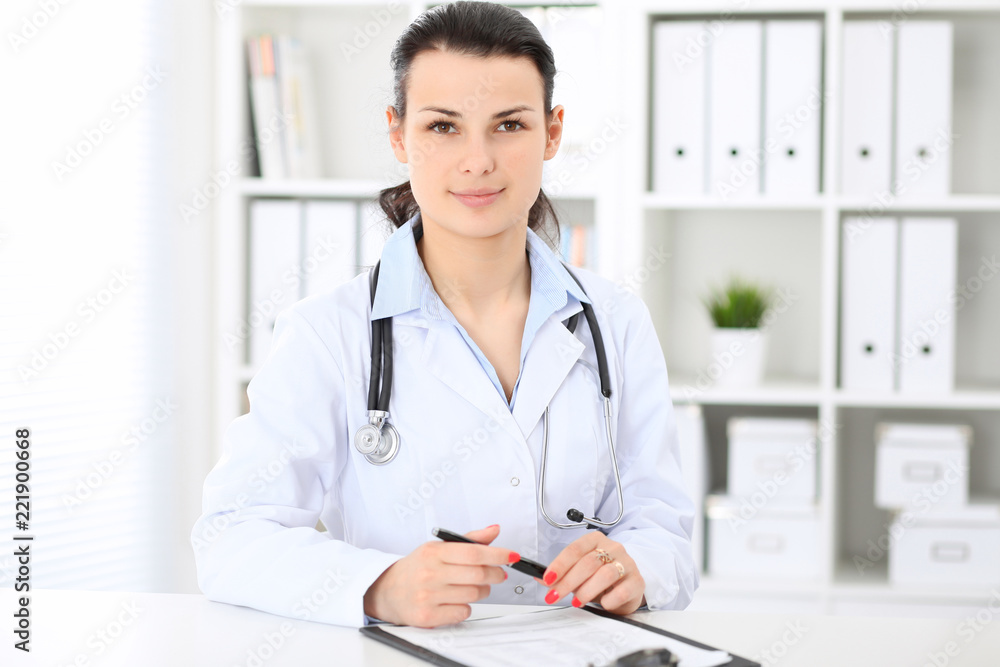 Young brunette female doctor at working place in hospital. Health care, insurance and help concept Young brunette female doctor at working place in hospital. Health care, insurance and help concept