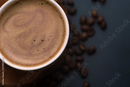Cappuccino coffee Cup on wooden stand and coffee beans on dark background