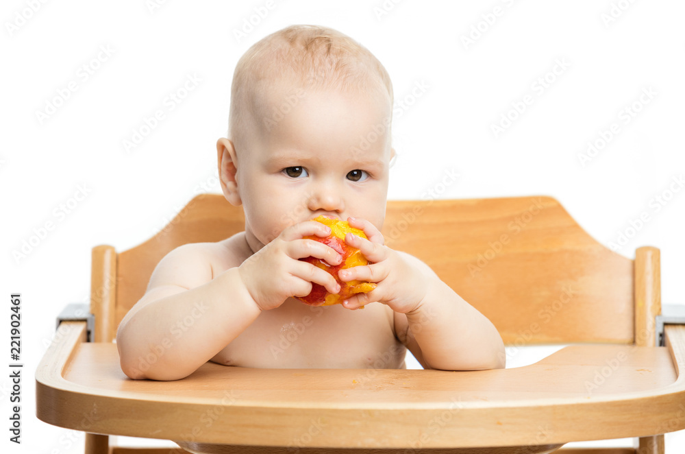 Cute baby girl eating peach while sitting in high chair over white Cute baby girl eating peach while sitting in high chair over white