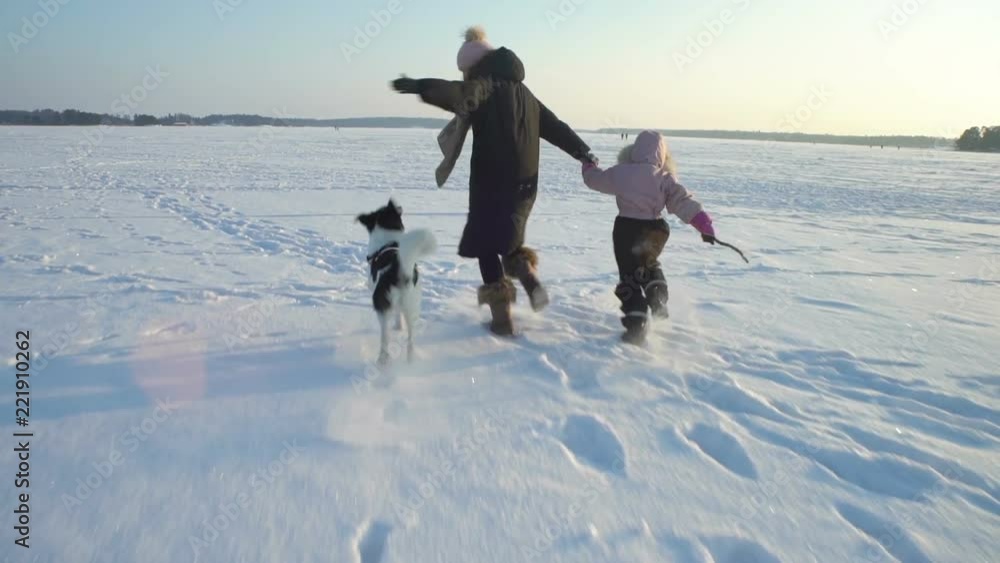 Winter fun snow vacation. Young woman with little girl and dog running on the ice of the frozen sea, lake in sunny day in Scandinavia. Slow motion