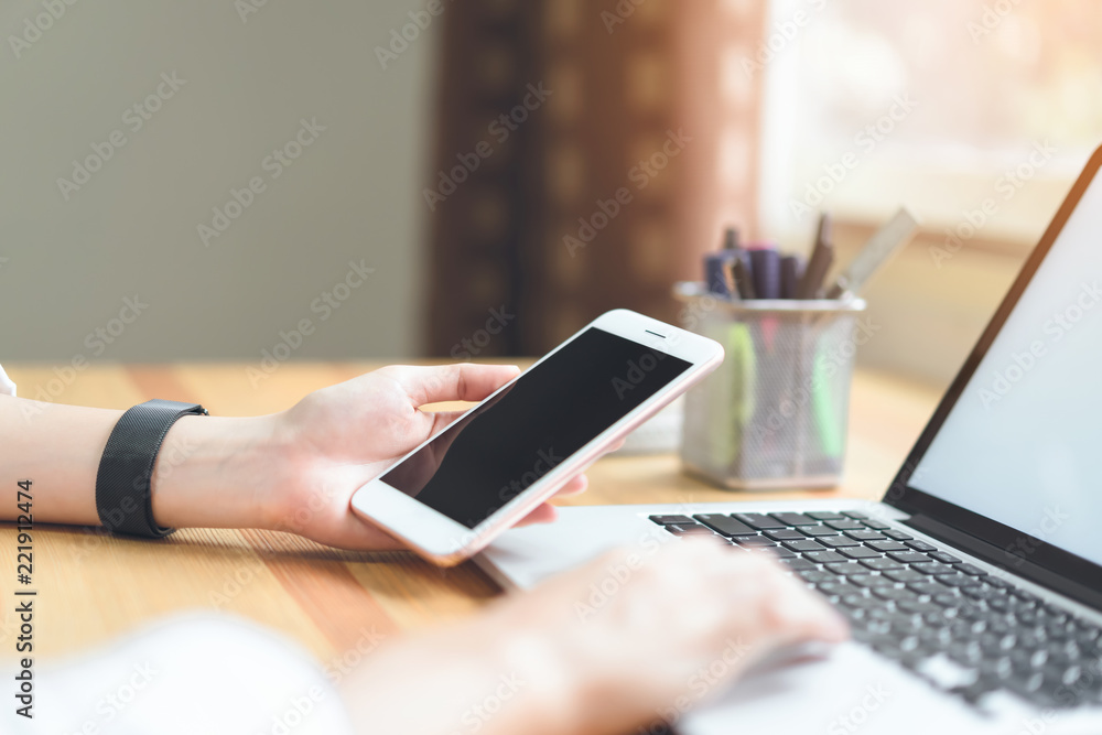 woman holding smartphone and using laptop on table in office room on windows with trees and nature background, for graphics display montage. Take your screen to put on advertising.