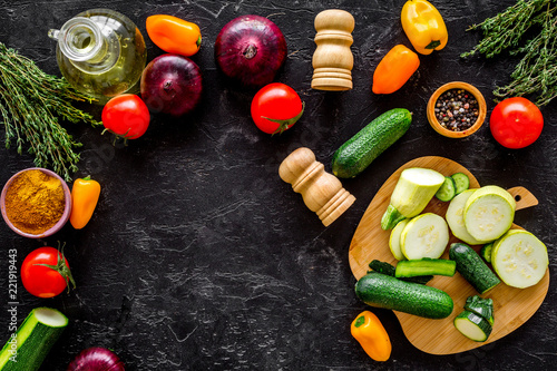 Cooking vegetable stew concept. Fresh vegetables squash, bell pepper, tomato, spices and cutting doard on black background top view space for text photo