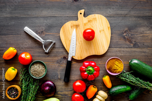 Cooking vegetable stew concept. Fresh vegetables squash, bell pepper, tomato, spices and cutting doard on dark wooden background top view copy space photo