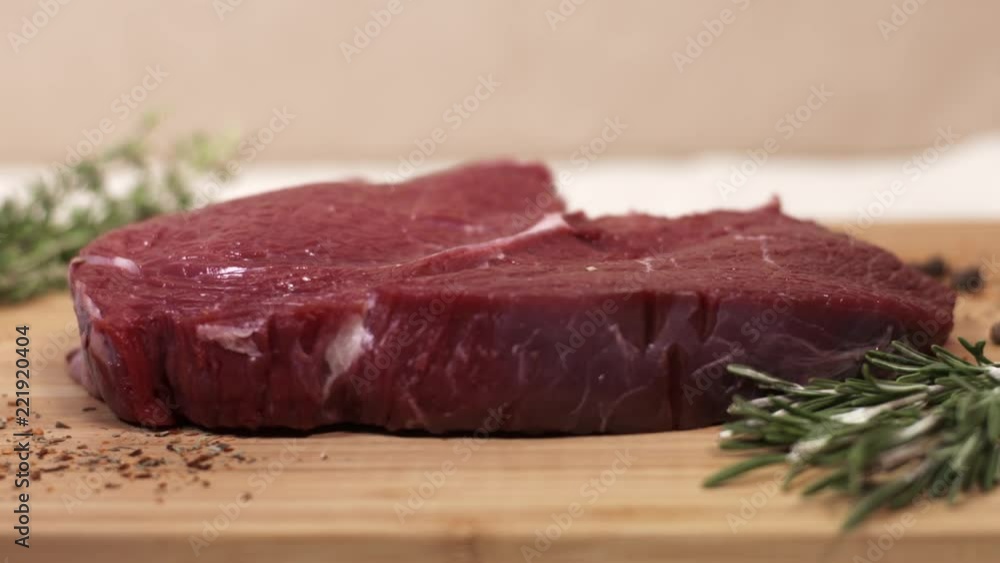 Piece of raw fresh red beef steak on table with rosemary and spices shadow of hand, close up Piece of raw fresh red beef steak on table with rosemary and spices shadow of hand, close up