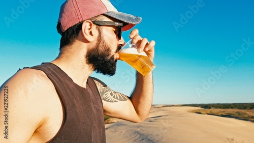 young man enjoying a cup glass of beer outdoor in the desert sand dunes