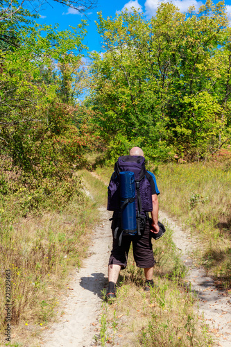 Backpacker hiking on the dirt road in green forest. Rear view